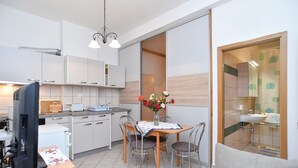 Een moderne keuken met witte kasten, een eettafel met stoelen, een tv op een standaard en een vaas met bloemen.