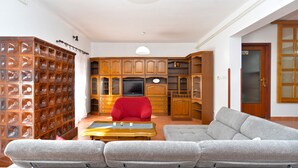 A living room with a grey sofa, a red armchair, a wooden cabinet with glass doors, and a television. - Apartment 1168 (Fazana)