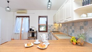 A kitchen with a wooden countertop, a coffee machine, a kettle, and a fruit bowl. There are two windows with curtains, a sink, and a stove. - Apartment 1168 (Fazana)