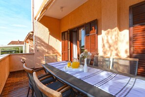 Een balkon met een tafel gedekt voor twee personen, met een karaf sinaasappelsap en een bloevas.