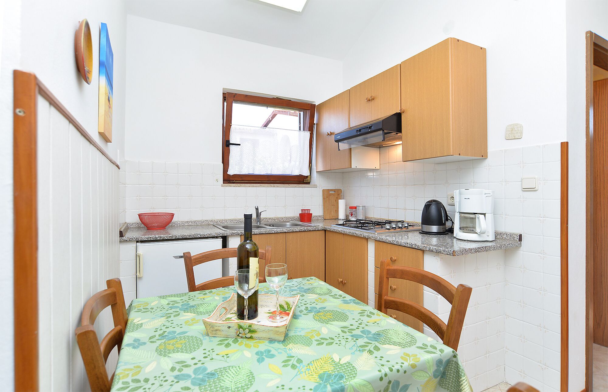 A compact kitchen with wooden cabinets, a gas stove, a coffee maker, and a dining table with chairs.