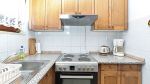 Cocina compacta con muebles de madera, estufa de acero inoxidable, cafetera y lavamanos.