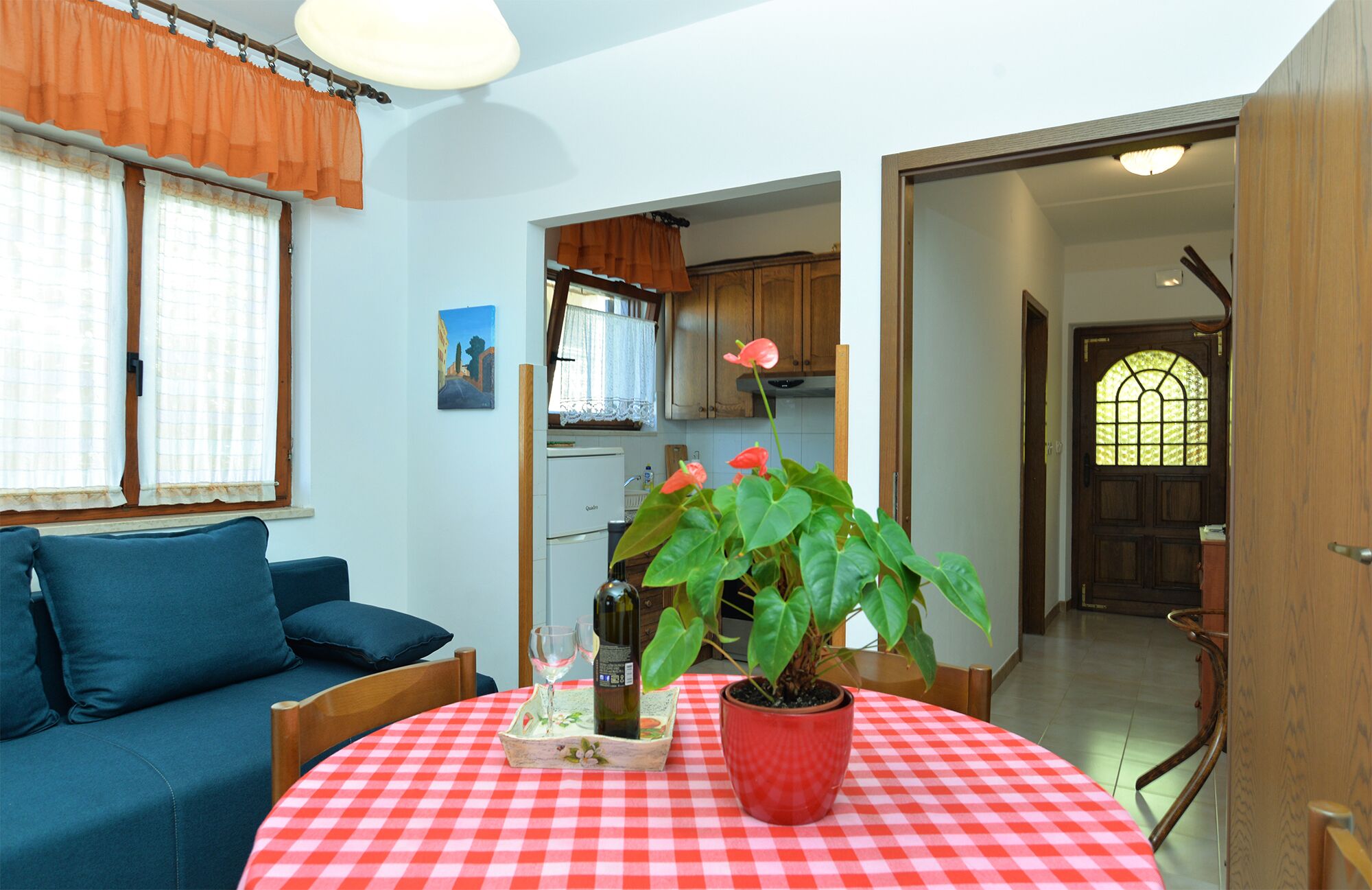 A living room with a blue sofa, a red and white checkered table, a potted plant, and a wine bottle.