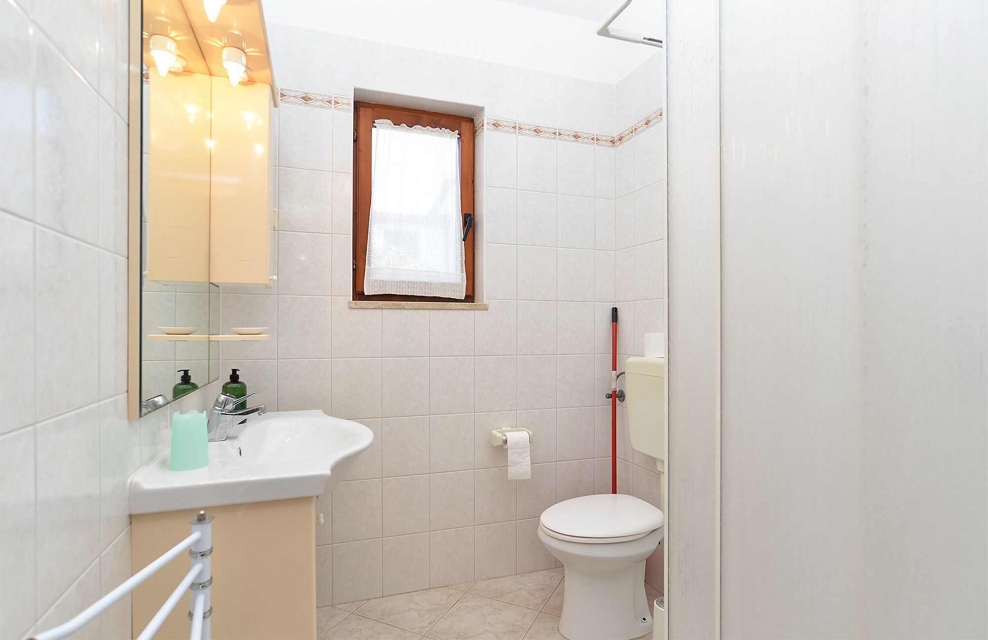 Une petite salle de bain avec des toilettes, un lavabo, un miroir et une fenêtre.