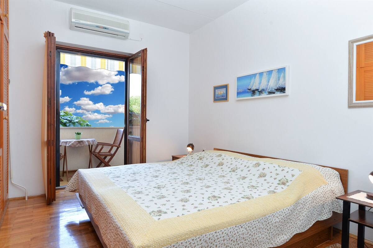 Une chambre à coucher avec un lit, une petite table, une chaise et une fenêtre donnant sur le ciel et les nuages.
