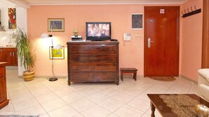 A living room with a wooden cabinet, a television, a small table, a plant, and a door with a no-smoking sign. - Apartment 1175 (Pula)