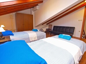 A room with two beds, a wooden ceiling, a wardrobe, and a sofa.