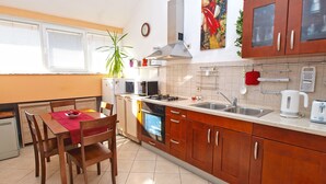 A compact kitchen with wooden cabinets, a dining table with chairs, a refrigerator, a stove, and a sink. - Apartment 1175 (Pula)