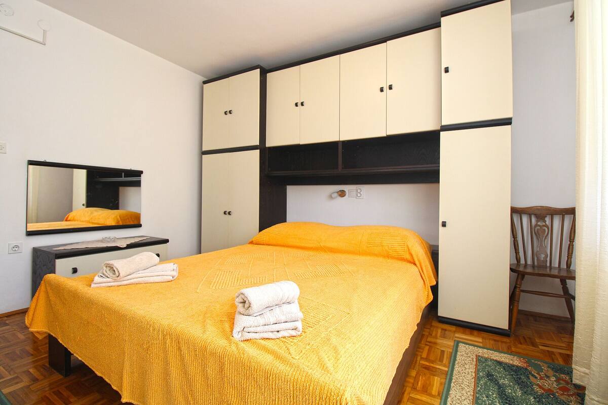 A bedroom with a bed, a wardrobe, a mirror, and a chair.