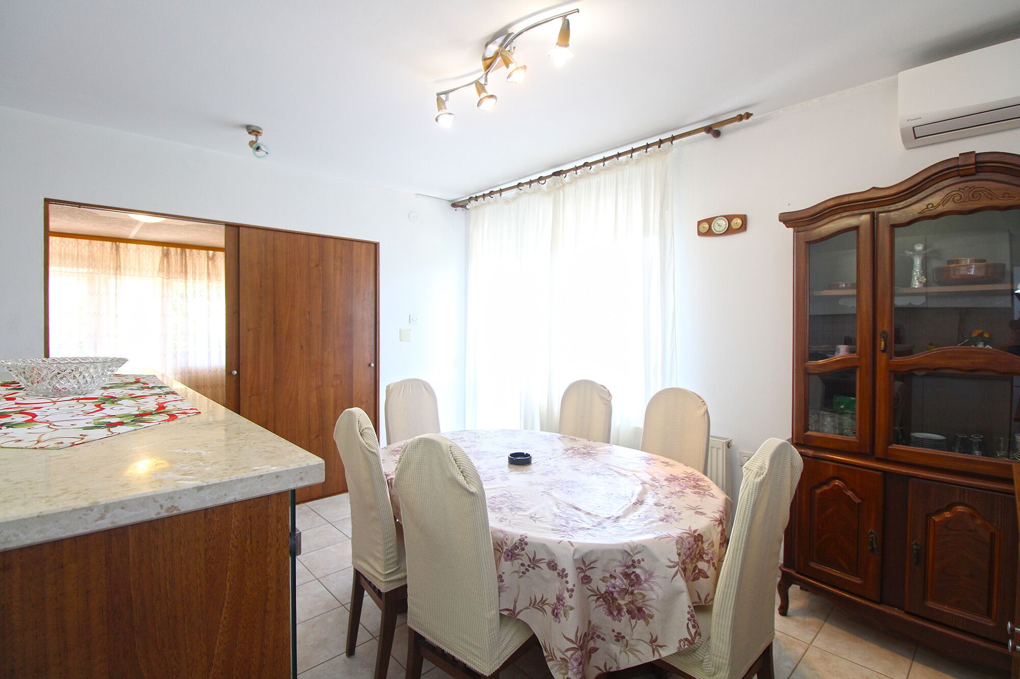 A dining area with a round table, six chairs, a wooden cabinet, and a kitchen island with a marble countertop.