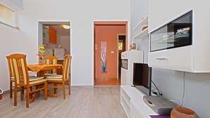 Ein kompakter Wohnbereich mit Essbereich, Fernseher und kleiner Küche, die durch eine offene Tür sichtbar ist.