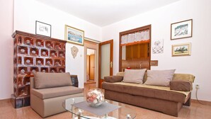 Ein Wohnzimmer mit einem Glastisch, zwei Sofas, einer Wand mit Dekoration und einer Tür zu einem weiteren Raum.