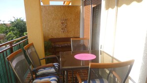 Ein Balkon mit Glastisch und Stühlen, einer kleinen Sitzecke und Blick auf Grünflächen.
