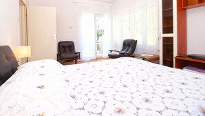 Une chambre d’hôtel dotée d’un grand lit, de deux fauteuils, d’un bureau, d’une armoire et d’une porte-fenêtre coulissante donnant sur un espace extérieur.