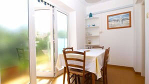 Un coin repas avec une table dressée pour quatre personnes, une porte-fenêtre coulissante donnant sur un balcon et une étagère ornée d’objets décoratifs.