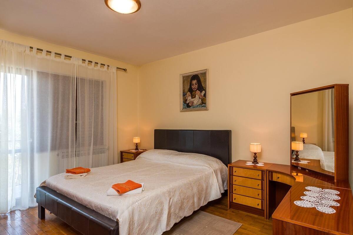 A bedroom with a bed, a nightstand, a dresser, a mirror, and a painting on the wall.