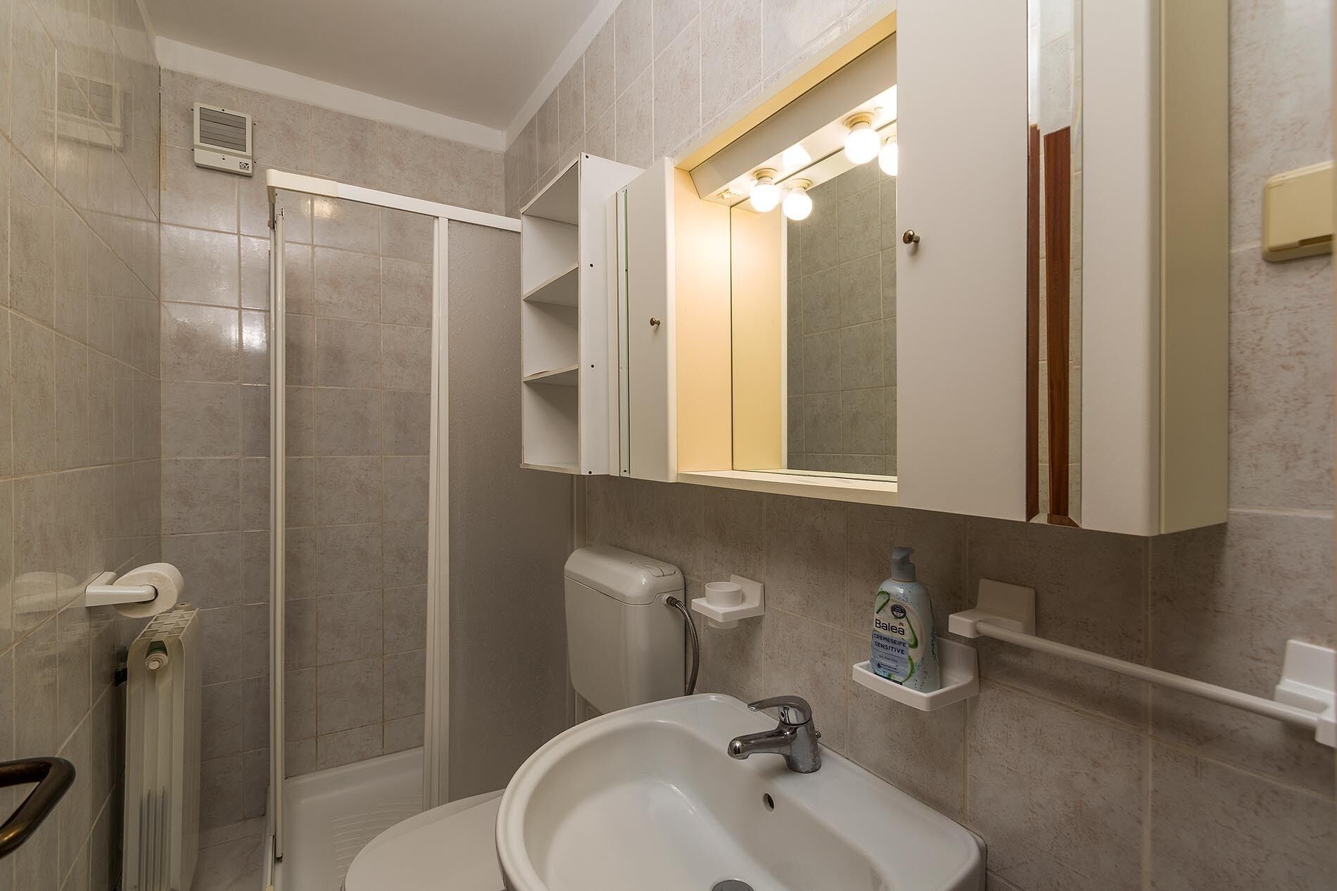 A bathroom with a shower, toilet, sink, and a mirror with lights.