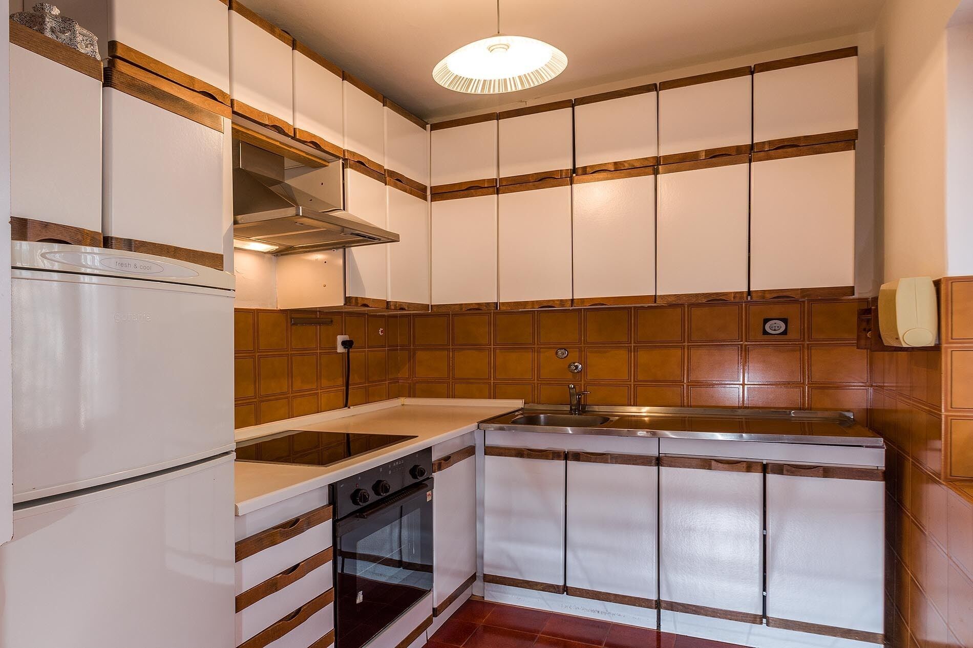 Eine kleine Küche mit weißen Schränken, einer Edelstahl-Spüle und einem eingebauten Backofen.