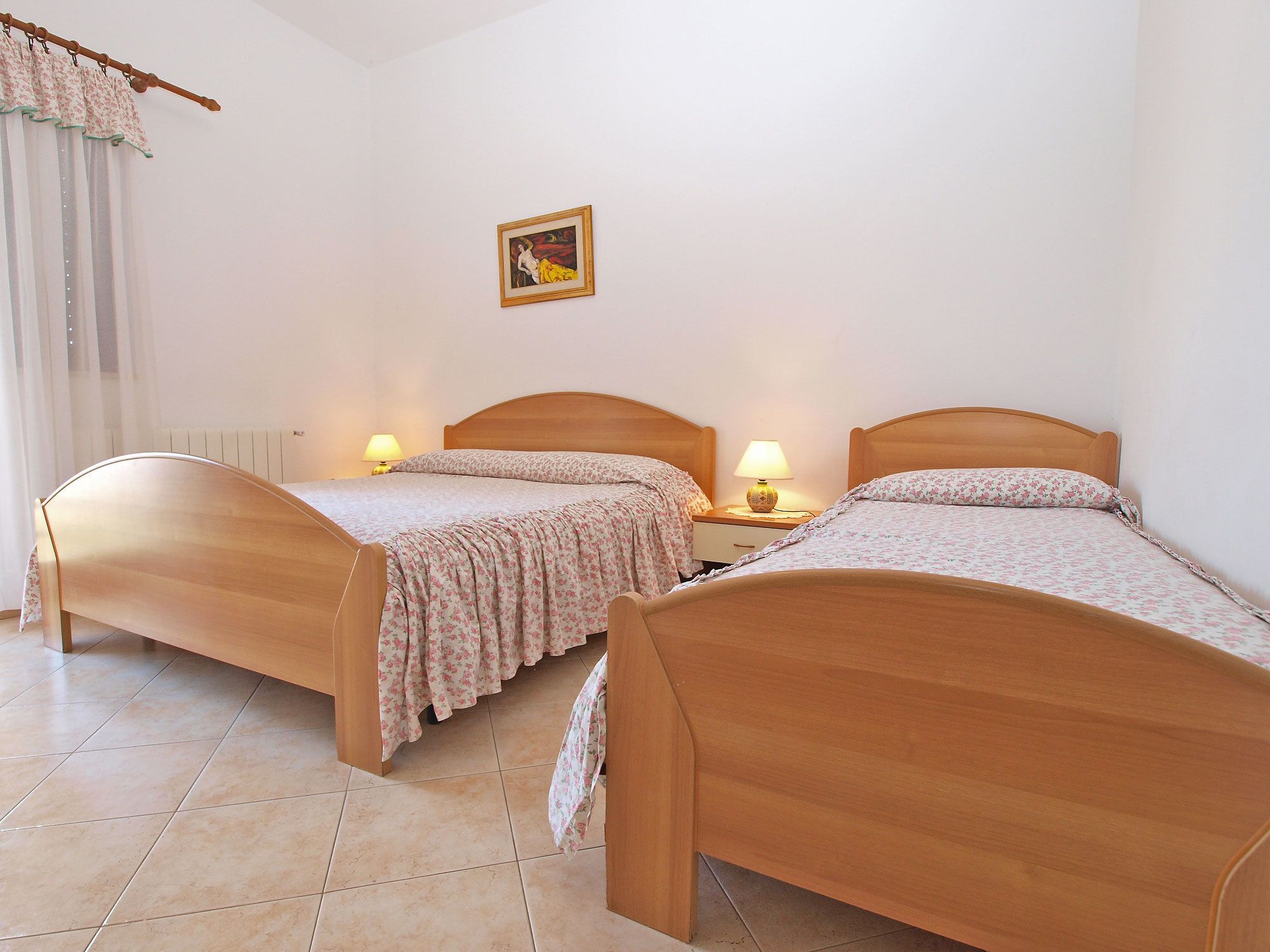 A bedroom with two wooden beds, a radiator, a wall-mounted picture, and a lamp on each nightstand.