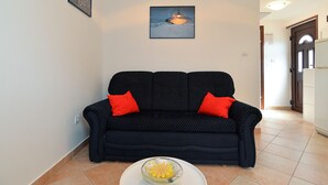 A living room with a black sofa, two red cushions, a glass bowl on a white table, and a painting on the wall. - Apartment 1203 (Pula)