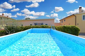 Une piscine à l’eau d’un bleu limpide, entourée de verdure et de bâtiments.