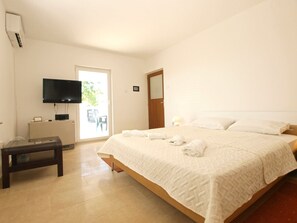 Un dormitorio con una cama, un televisor montado en la pared, una mesita y una puerta que da a un balcón.