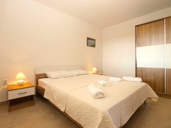 Una cama bien hecha con cubrecama acolchada, dos lámparas de noche, una mesita de noche con cajón y un armario de madera.