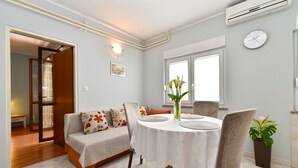 A dining area with a round table, chairs, a sofa with floral cushions, a potted plant, and a clock on the wall. - Apartment 1230 (Pula)