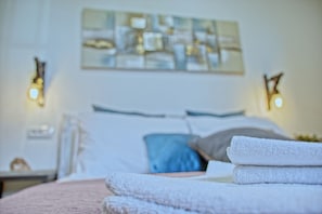 A neatly made bed with white linens and a blue pillow, a wall-mounted abstract painting, and two bedside lamps. - House 1231 (Pula)
