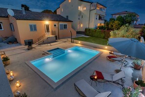 A swimming pool with steps leading into it, surrounded by lounge chairs and a small table with a candle.