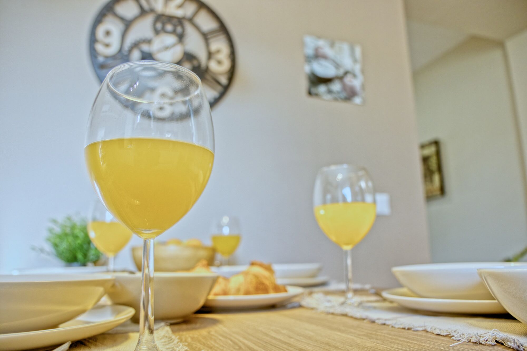 Una mesa de comedor con dos vasos de una bebida amarilla, platos y un reloj en la pared.