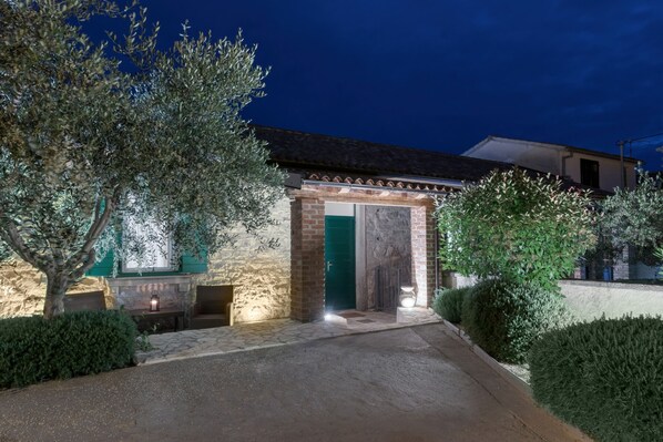 A stone building with a green door, a paved entrance, and a well-lit pathway.