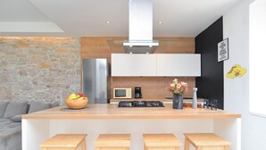 A modern kitchen with a central island, a stone wall, and a blackboard with motivational writing. - House 1231 (Pula)