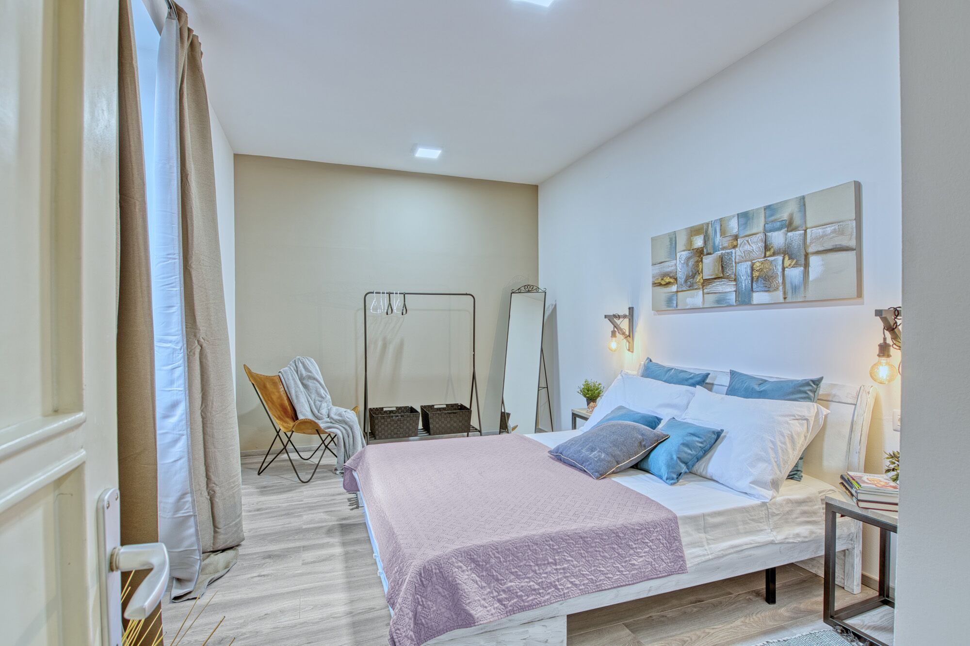 Une chambre à coucher comprenant un lit, une chaise, un miroir et une œuvre d’art accrochée au mur.