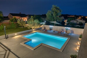 A rectangular swimming pool with a tiled edge, surrounded by a concrete deck. There are lounge chairs and a small table with a fire feature. - House 1231 (Pula)