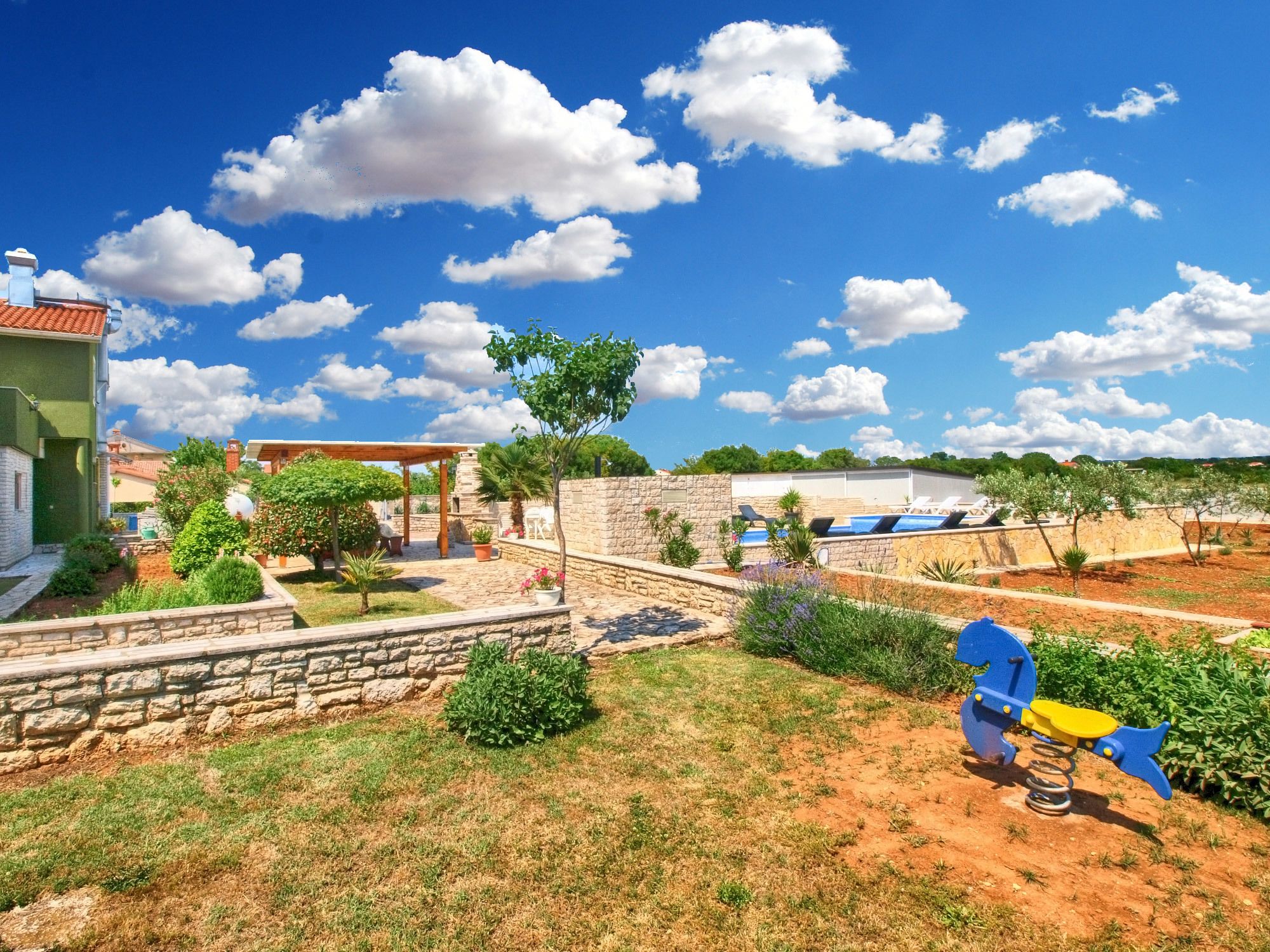 A residential area with a stone wall, a wooden pergola, and a playground with a swing set.