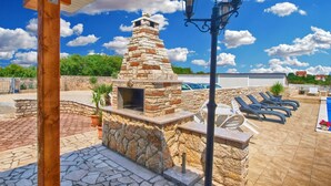 An outdoor patio with a stone barbecue grill, lounge chairs, and a pergola structure. - Apartment 1376 (Fazana)