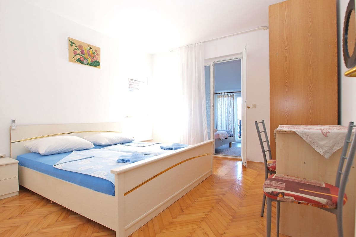 A bedroom with a bed, a chair, a wardrobe, and a door leading to another room.