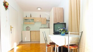 A compact kitchen with wooden cabinets, a small refrigerator, and a television. - Apartment 1265 (Fazana)