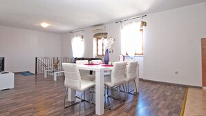 A spacious dining area with a white table and chairs, a staircase, and a view of the outdoors. - House 1277 (Visnjan)