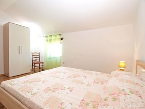 Un dormitorio con cama, armario, silla y mesita de noche con lámpara.