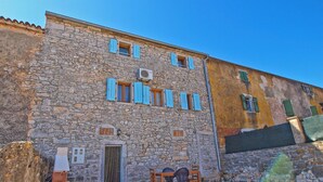 A stone building with a door and windows, a small outdoor seating area with tables and chairs, and a gravel path. - House 1277 (Visnjan)