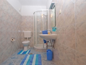 Baño con inodoro, lavamanos, ducha y alfombras a rayas azules.