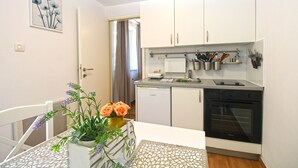 A compact kitchen with white cabinets, a dishwasher, and an oven. There is a dining table with a vase of flowers. - Apartment 1278 (Pula)