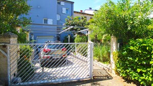 A gated residential area with a parked car, a blue building, and lush greenery. - Apartment 1278 (Pula)
