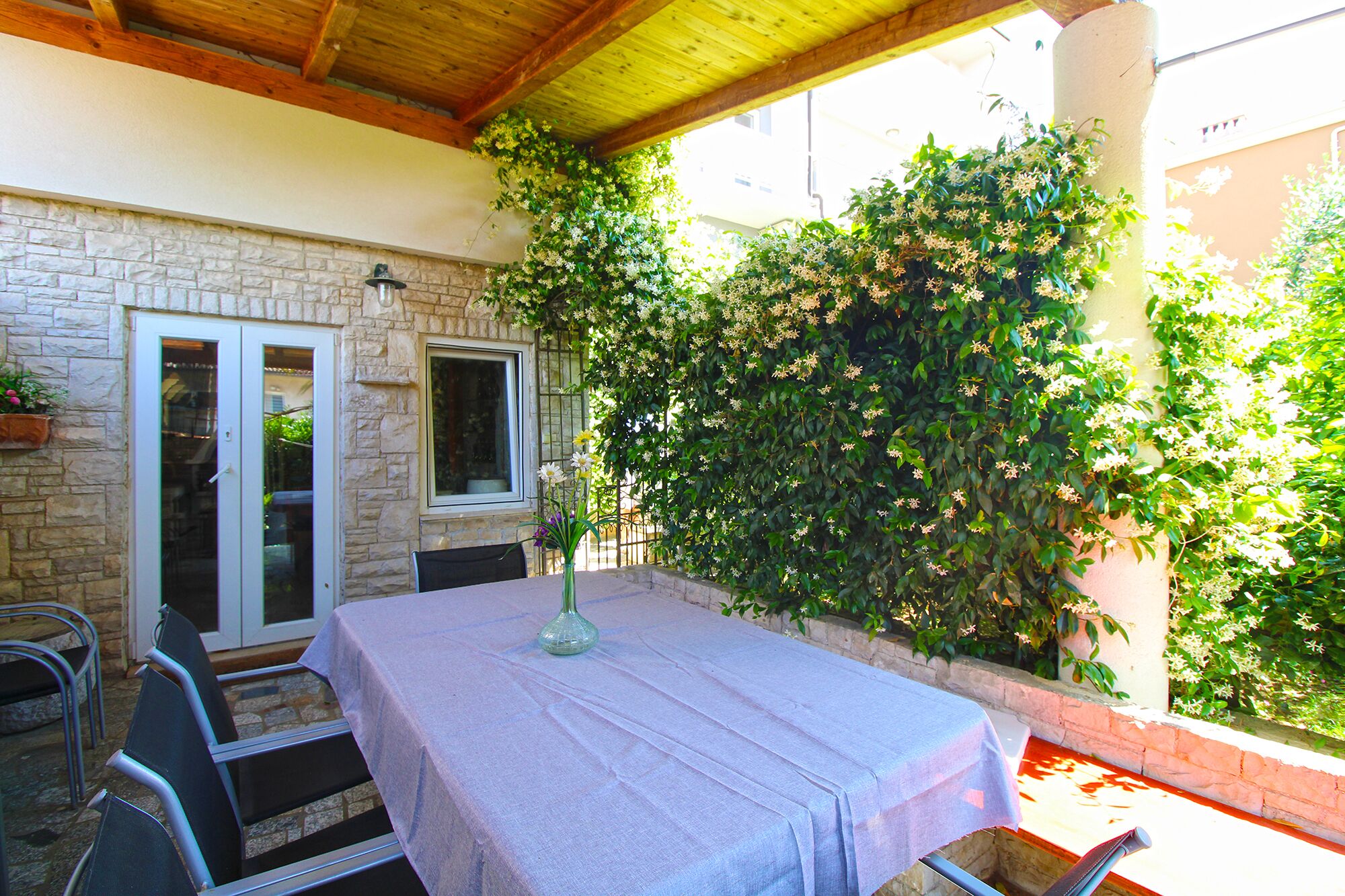 An outdoor patio with a table and chairs, a stone wall, and a covered area with a wooden ceiling.