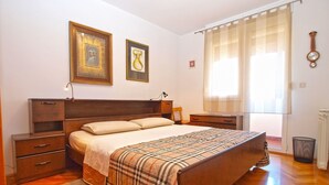 A bedroom with a wooden bed, bedside tables, a nightstand, a window with curtains, and a wall clock. - Apartment 1286 (Pula)