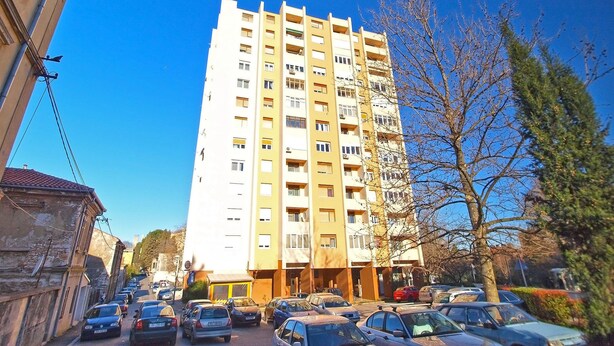 A multi-story residential building with a central entrance, parking area, and adjacent trees. - Apartment 1286 (Pula)