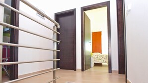 Ein Flur mit Metallgeländer, einer Holztür und einem Bett mit floralem Überwurf im Hintergrund.