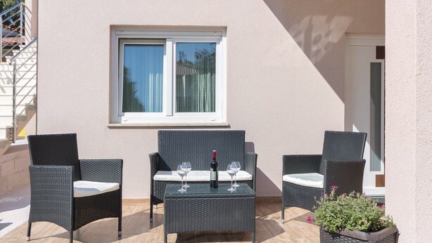 Eine Terrasse mit Korbmöbeln, einem Tisch und einer Weinflasche.
